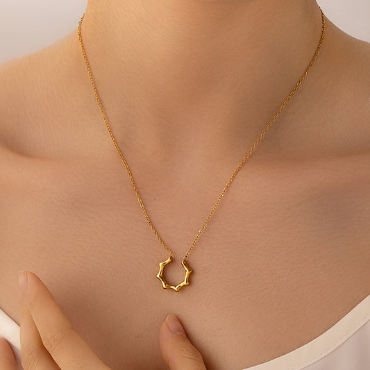 A delicate gold chain necklace with a small, textured open hexagonal pendant, shown worn on a model's neck with a hand gently resting near the chest.