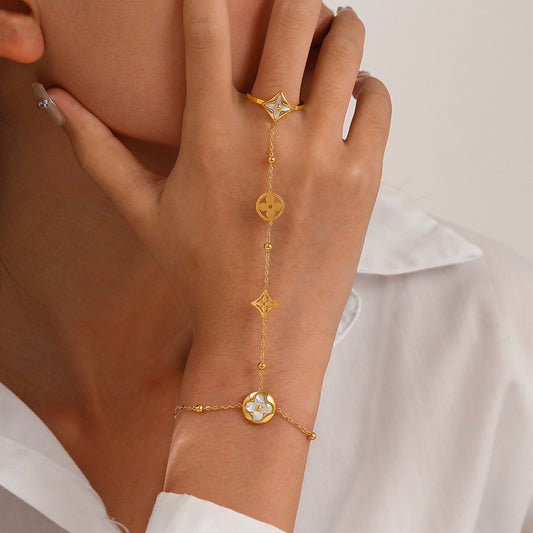 A delicate gold chain jewelry set worn on a model's hand and wrist, featuring a ring with a star-shaped clear stone, a matching bracelet with a flower-shaped clear stone, and a central chain with circular and star motifs, all set against a white shirt and a light background.