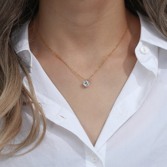 Gold necklace with a diamond pendant worn by a person in a white shirt.