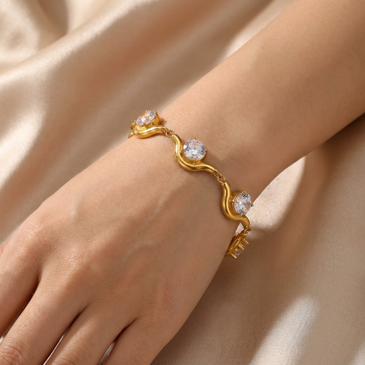 A gold chain bracelet with bezel-set round clear stones, styled on a hand.