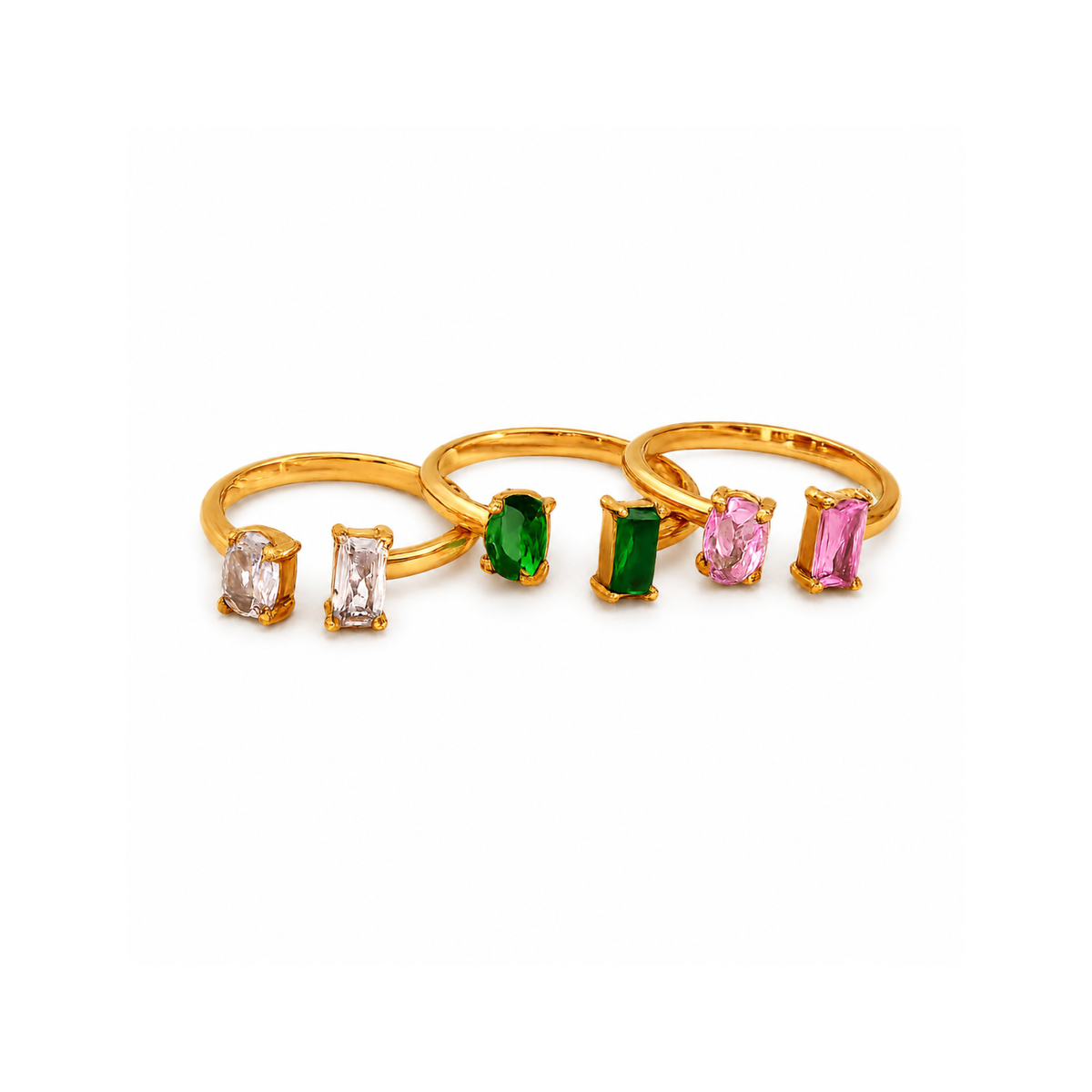 Three gold rings with rectangular  and oval gemstones in clear, green, and pink, arranged in a row on a white background.