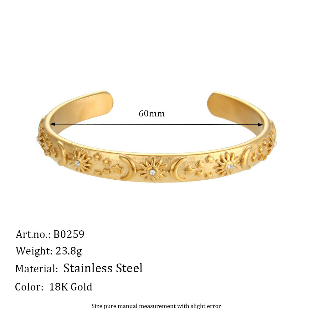 Gold-toned stainless steel Celestial Star, Moon & Sun Bangle shown on a white background with a 60mm size indicator and product details text below.