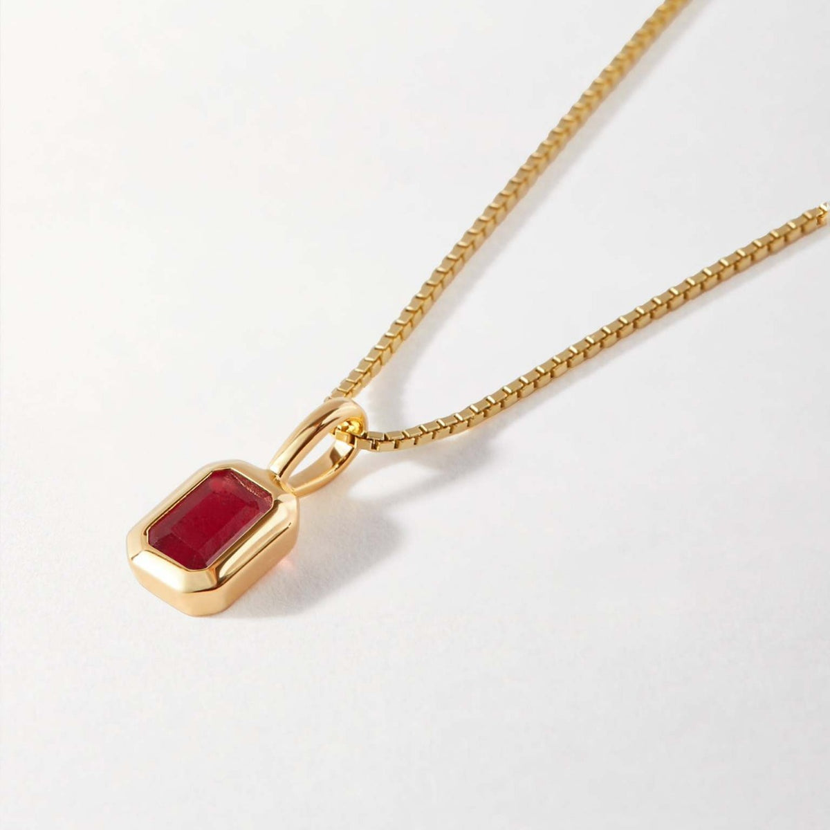 Gold Birthstone necklace with a red pendant on a light gray background