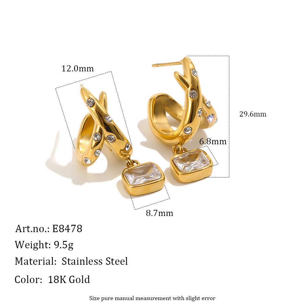 Gold-tone stainless steel huggie hoop earrings with rectangular clear crystal drops and small clear rhinestone accents, shown with dimension callouts and product text on a white background.