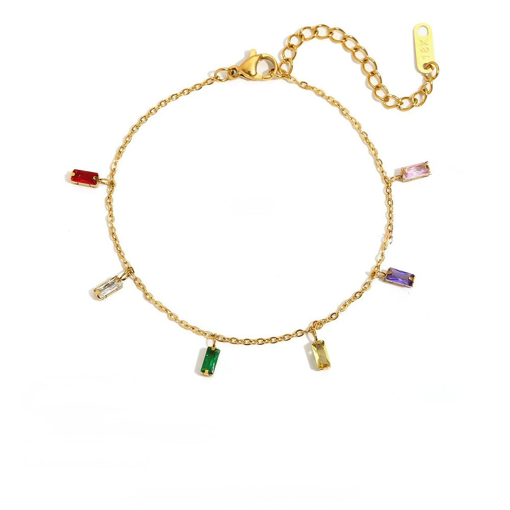 A gold chain bracelet with seven small rectangular baguette gemstones in various colors (red, pink, purple, green, yellow, clear, and silver-toned) arranged in a circle on a white background.
