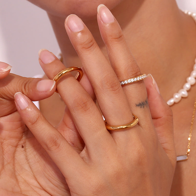 Close-up of a person's hands styling Trio of elegance ring set, with a pearl necklace visible in the background.
