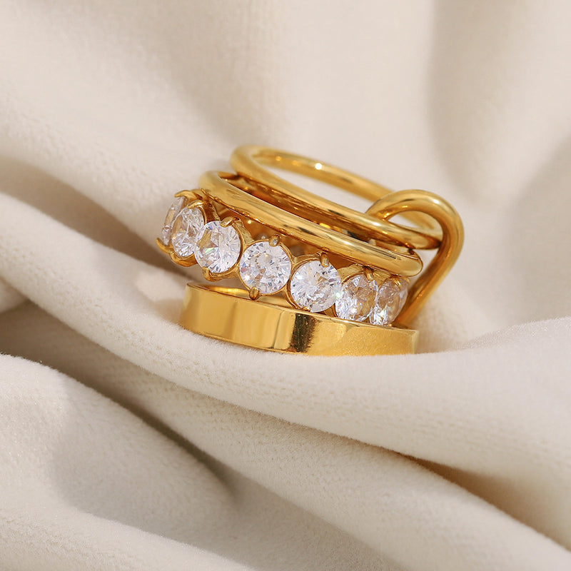 A gold ring set with five clear round-cut gemstones, displayed on draped cream-colored fabric.