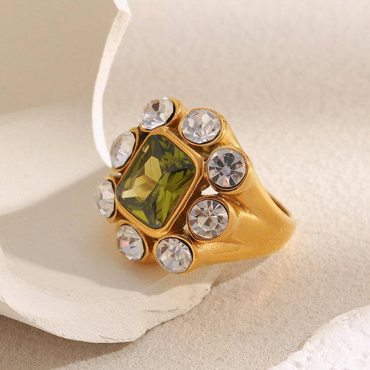 Gold ring with green gemstone and clear crystals on a textured beige background