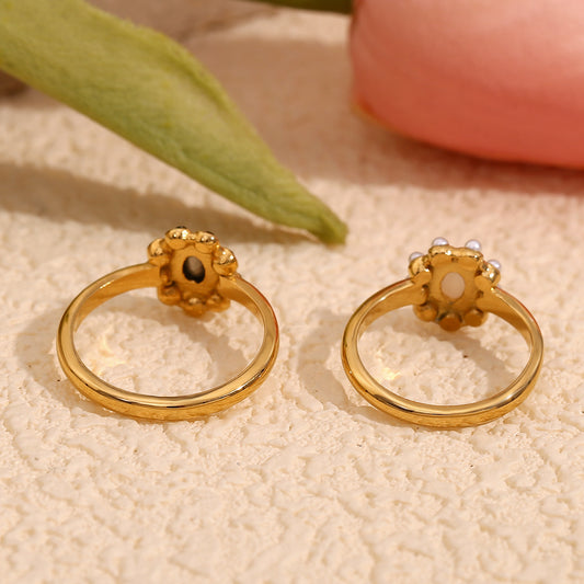 Rear view of gold flower-shaped rings displayed on a textured cream surface with soft decorative background elements.