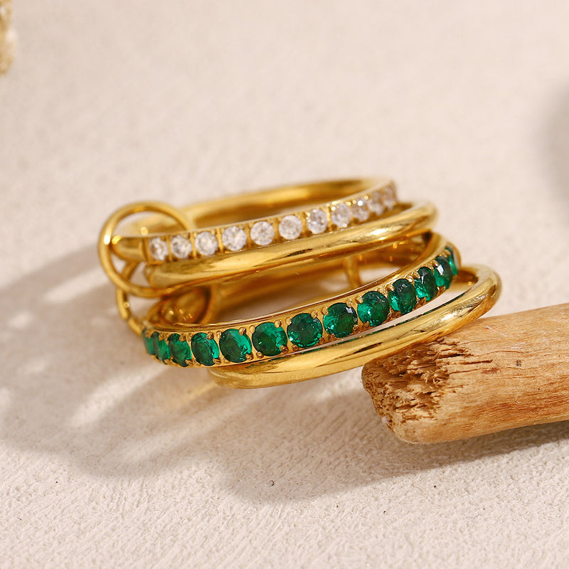 Gold ring with emeralds and diamonds on a wooden stick against a beige background