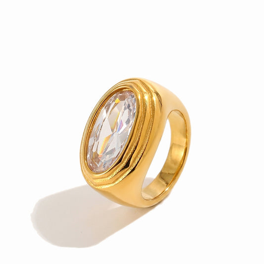 A gold signet-style ring with a large oval clear faceted gemstone, shown on a clean white background with a soft shadow.