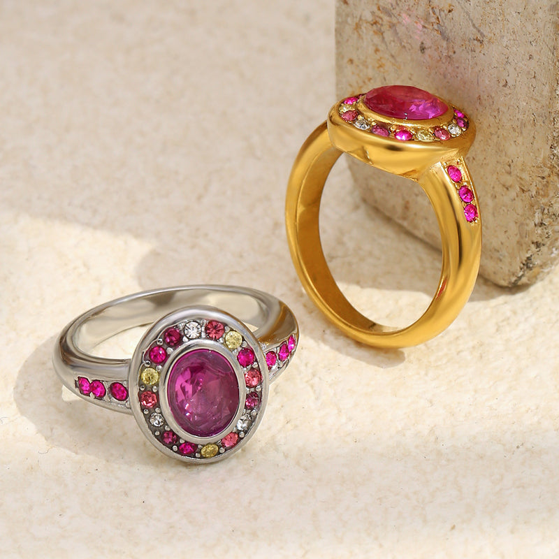 Two rings, one gold and one silver, each with a pink gemstone on a textured beige surface.