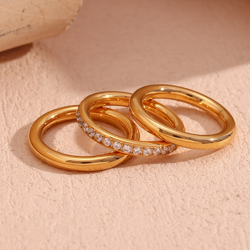 Three gold rings with diamond accents on a light pink background