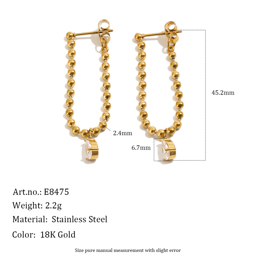Gold-toned stainless steel beaded drop earrings with a small clear faceted stone at the bottom, shown on a white background with measurement annotations and product details text below.
