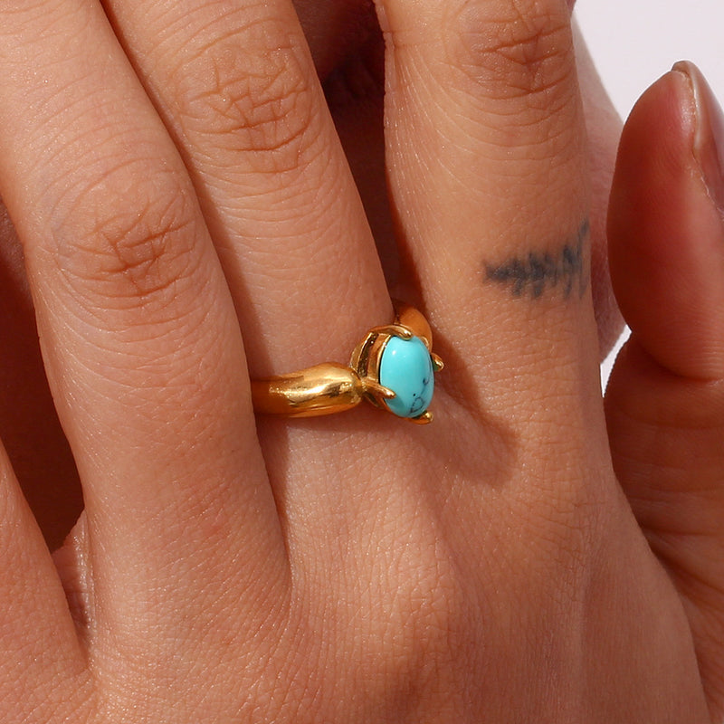 A gold ring with a round turquoise cabochon gemstone, worn on a person's finger.