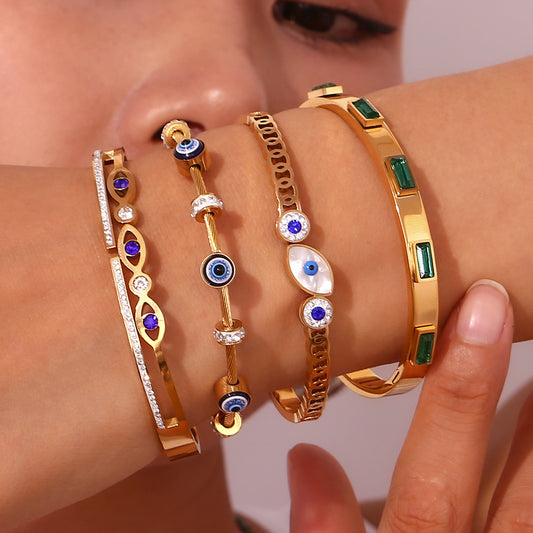 A close-up of a person's wrist wearing five gold-toned bracelets with blue, white, and green details.