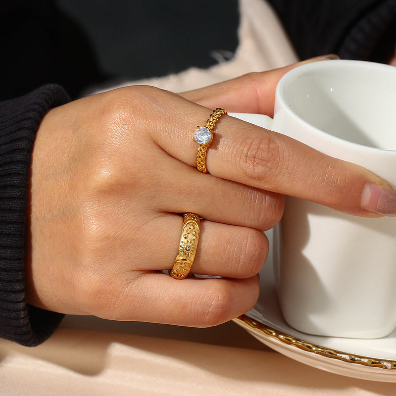 Hand wearing gold rings holding a white mug with a beige background