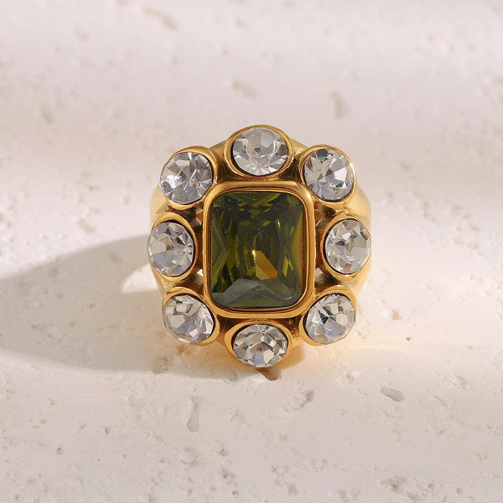 Gold ring with a green gemstone and clear crystals on a light background