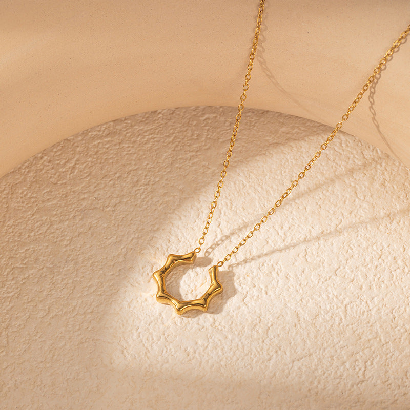 A gold necklace with a textured, wavy open circle pendant, displayed on a textured beige surface with soft shadows.