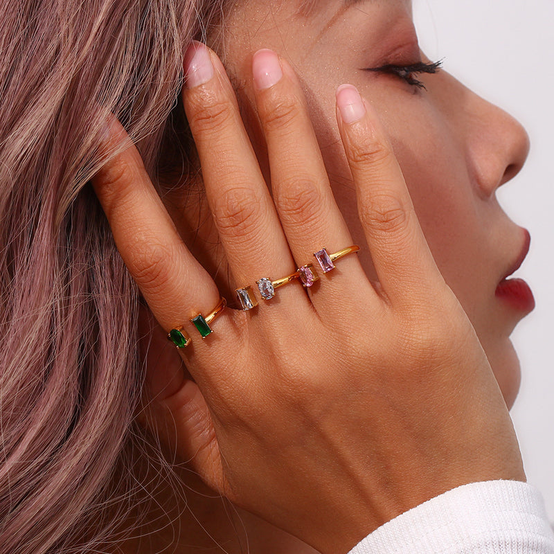 Close-up of a hand wearing a gold ring with colorful gemstones, held near the face.