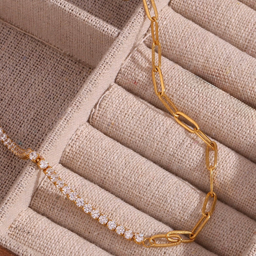 A gold chain necklace with a row of clear cubic zirconia stones, displayed on a beige textured jewelry organizer tray.