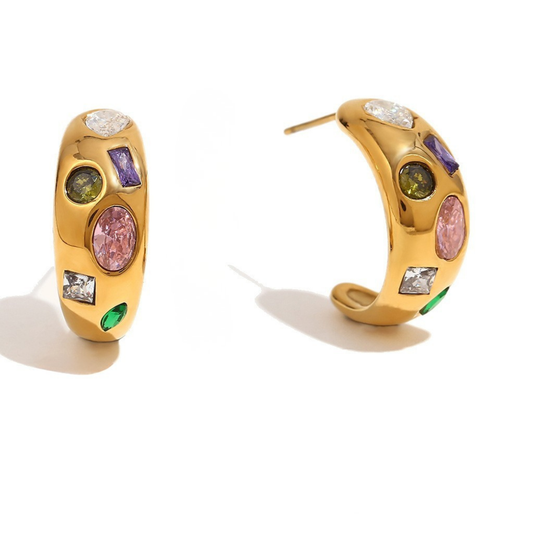 A pair of gold huggie hoop earrings decorated with colorful gemstones, including pink, purple, green, and clear stones, displayed on a clean white background.