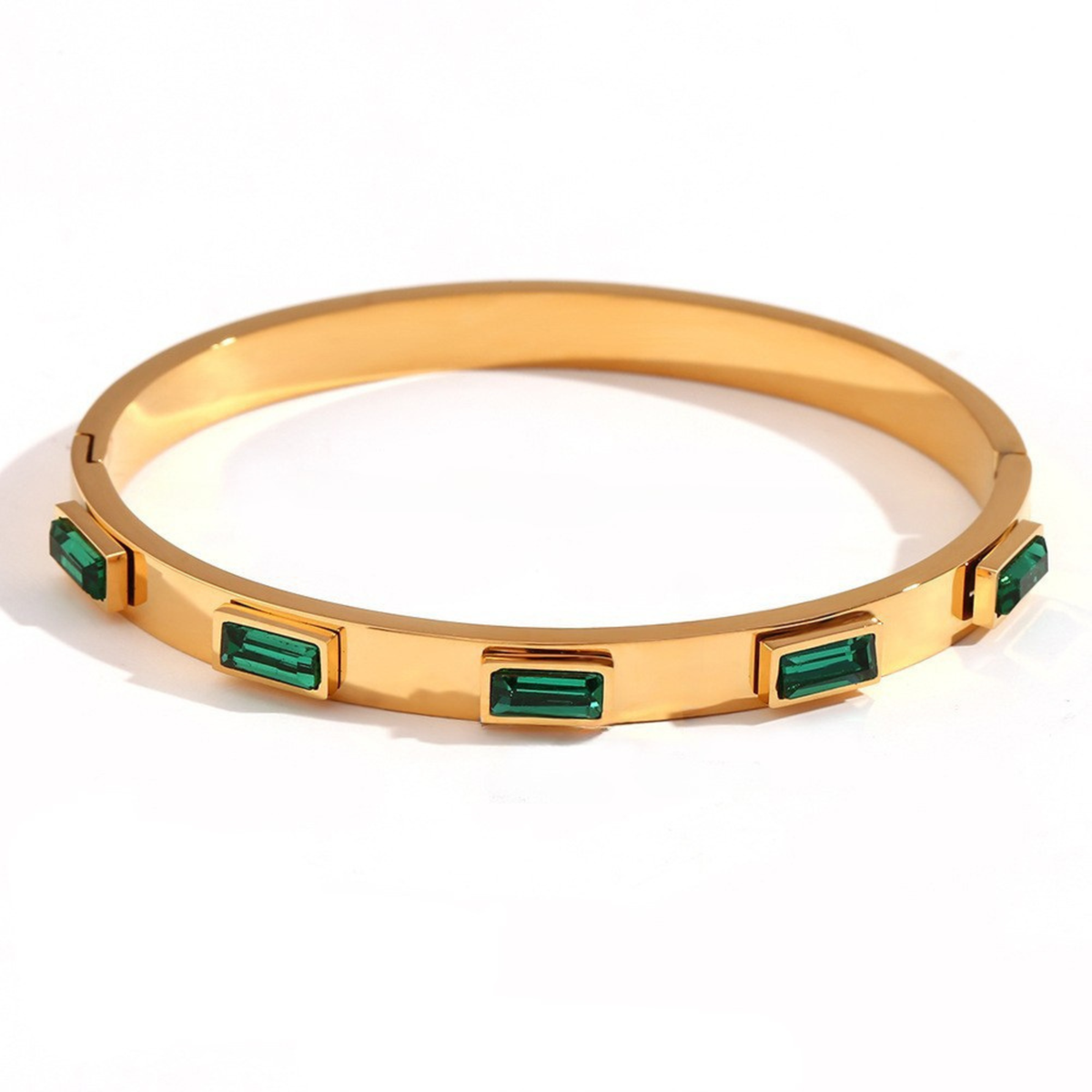 A gold bangle bracelet featuring five rectangular green emerald-cut gemstones spaced evenly around the band, set against a plain white background.