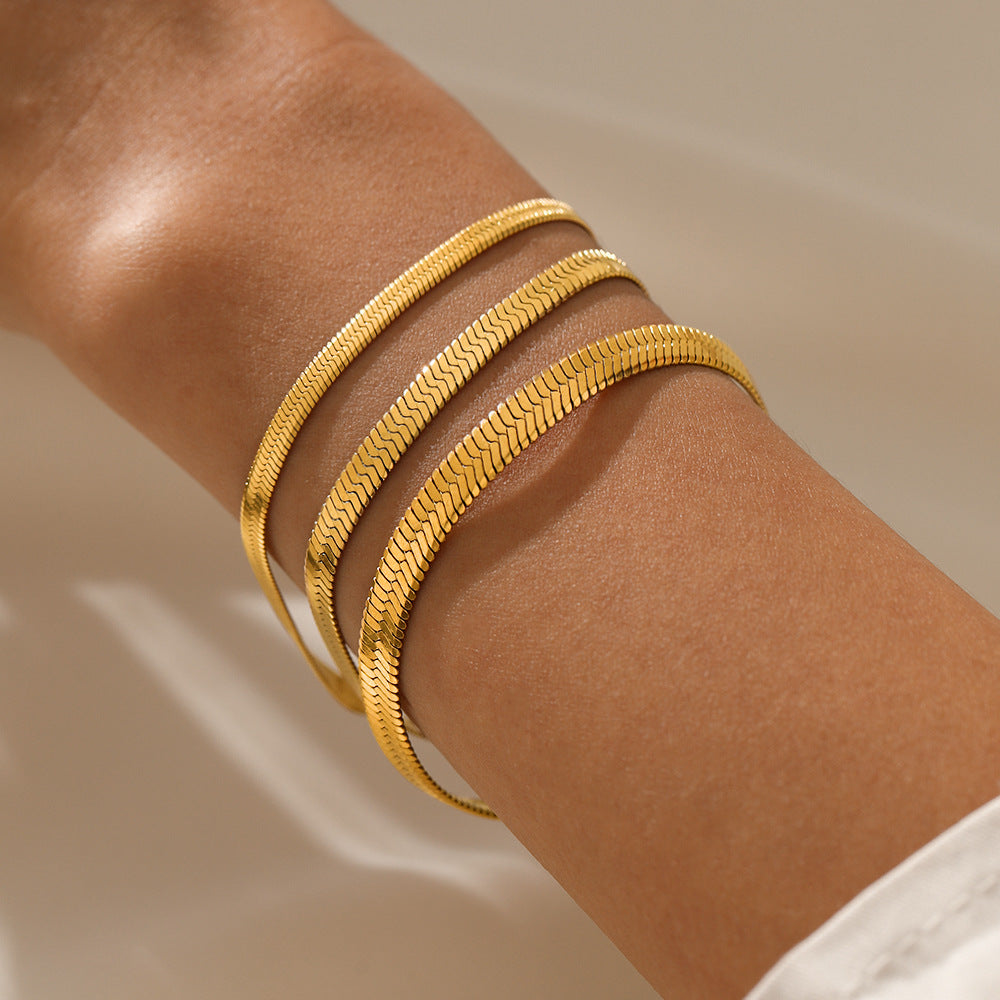 Gold bracelets on a person's wrist against a neutral background