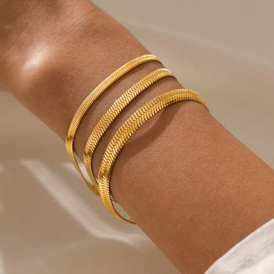 Gold bracelets on a person's wrist against a neutral background
