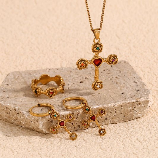 Gold jewelry set with cross pendant, rings, and earrings on a stone surface.
